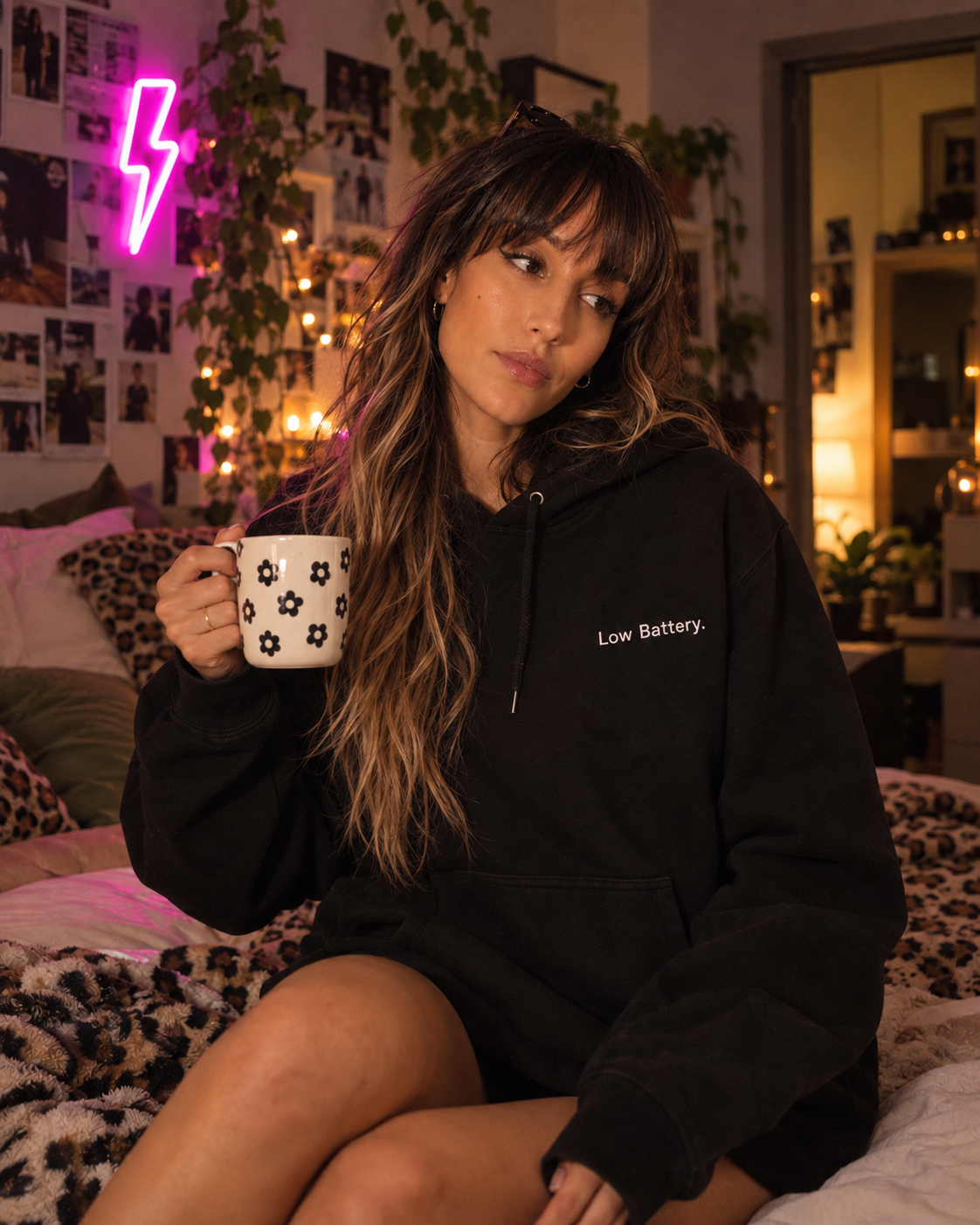 Woman sitting on a bed in the black Low Battery. embroidered hoodie