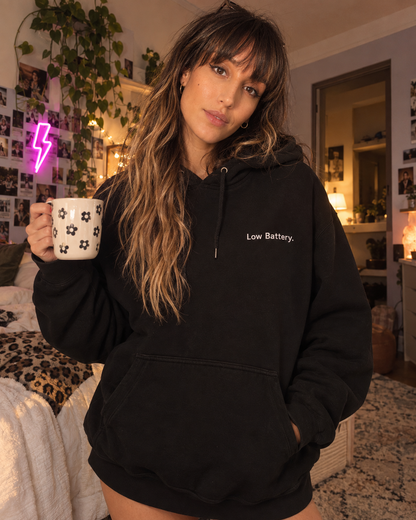 Woman wearing the Low Battery. embroidered hoodie in Black, holding a mug