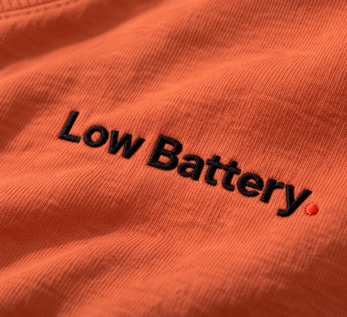 Close-up of the Low Battery. embroidery with orange-red full stop on Terracotta fabric