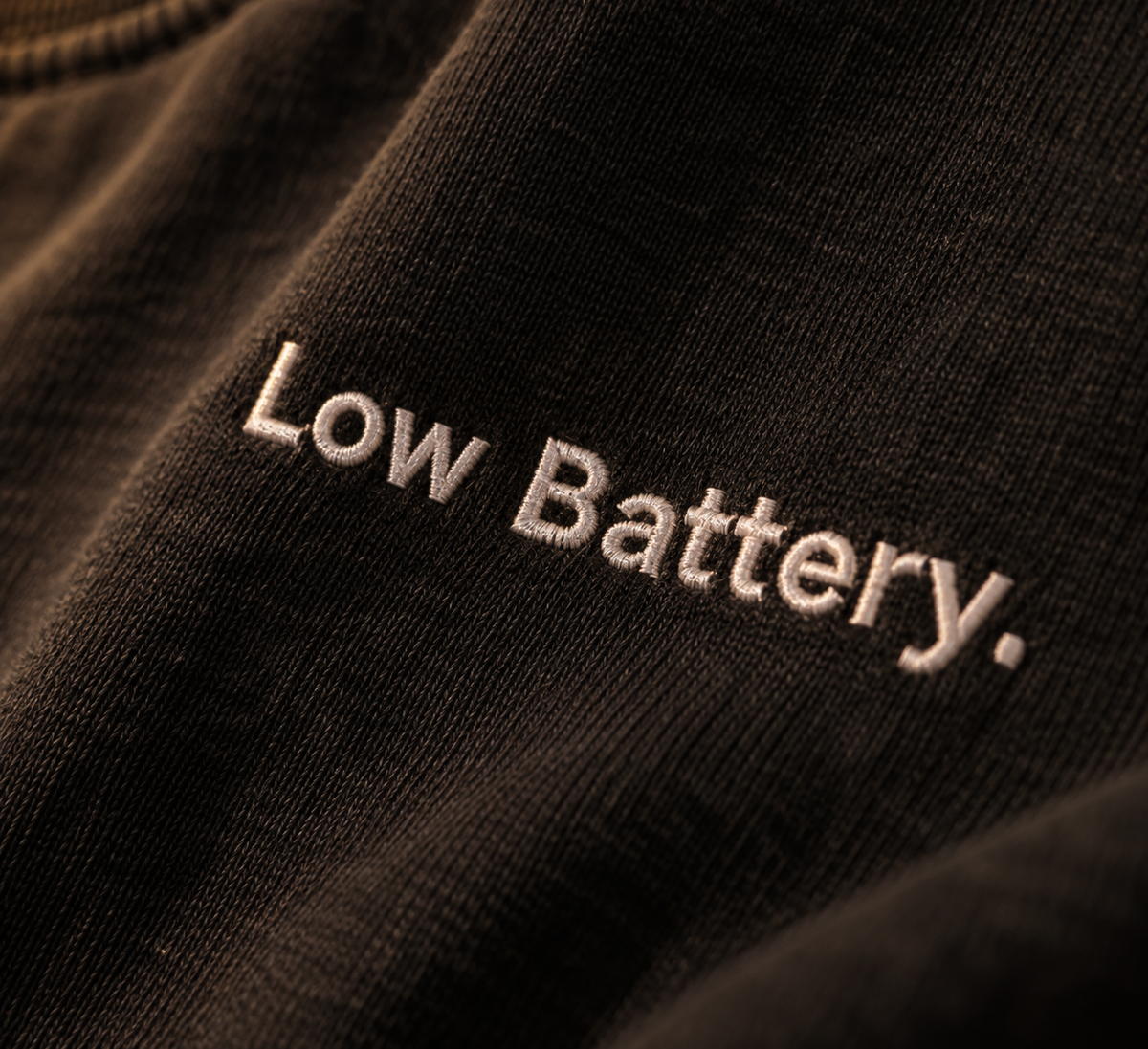 Close-up of white Low Battery. embroidery on Washed Black fabric