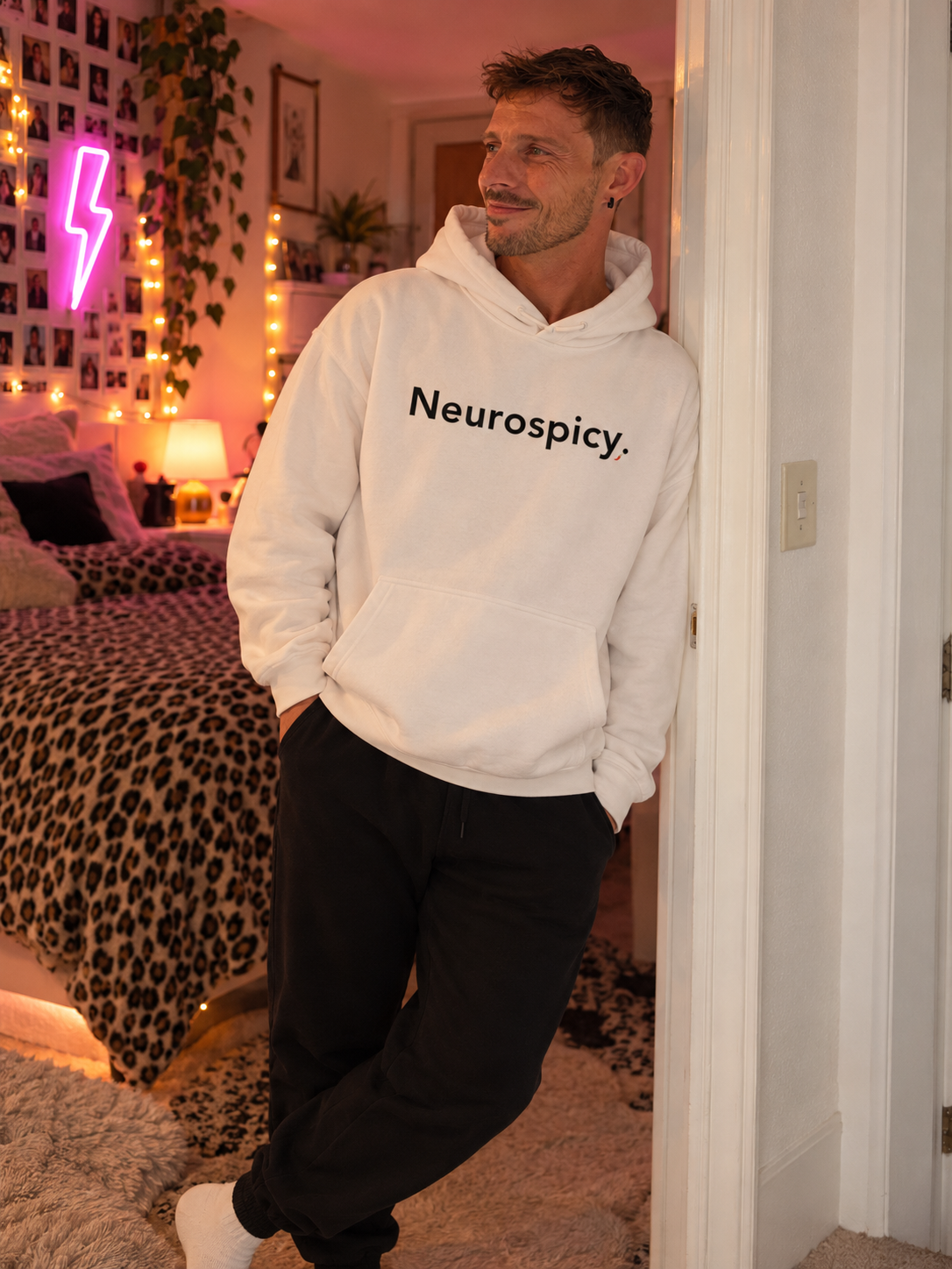 Man wearing the white Neurospicy. hoodie, leaning in a bedroom doorway